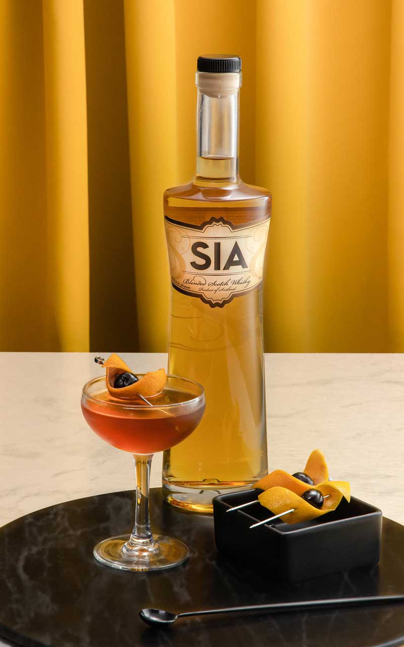 A bottle of SIA Blended Scotch Whisky behind a Manhattan martini made with SIA