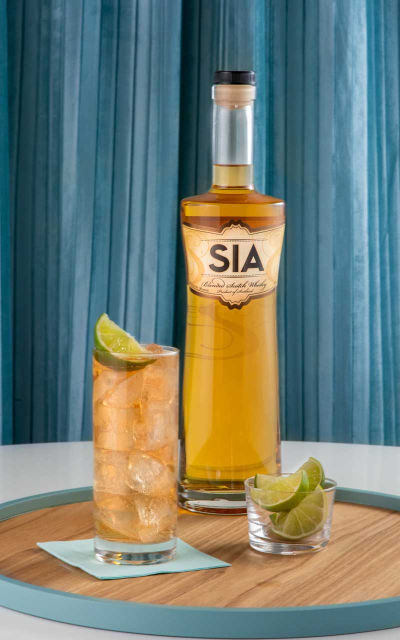 A bottle of SIA Blended Scotch Wisky behind a SIA Ginger cocktail