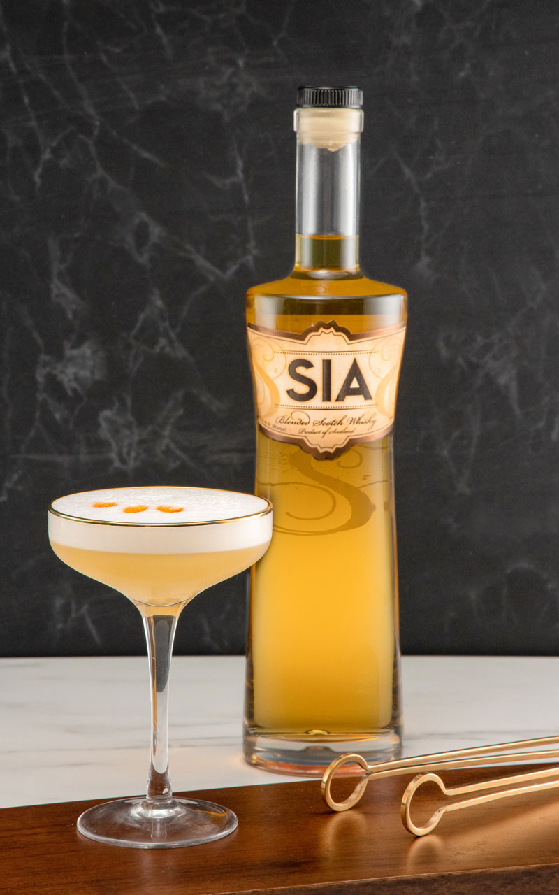 A bottle of SIA Blended Scotch Wisky behind a SIA Whisky Sour cocktail